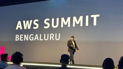 Prashant Akhawat walking the stage in front of the AWS Summit Bengaluru title wall.